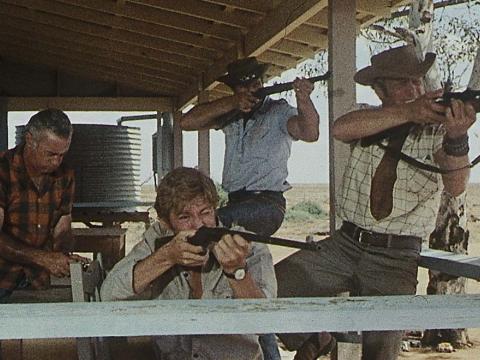 Four men on an outback verandah, three of whom are aiming their rifles at something unseen