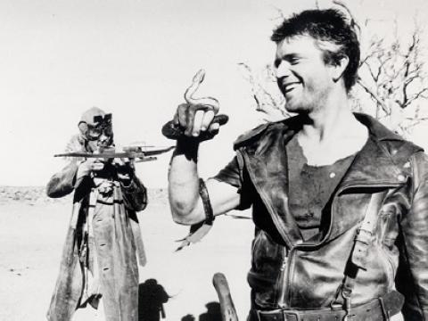 Max (Mel Gibson) holds a snakes while the Gyro Captain (Bruce Spence) points a crossbow at him