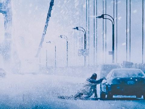 A man slumped next to his car on a frozen bridge in the snow.