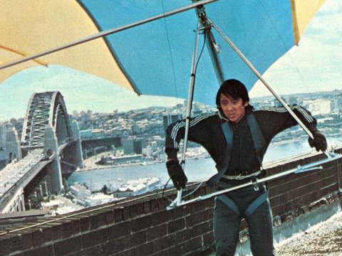 Image of a man getting set to hang glide off a tall building. In the background you can see the Sydney Harbour Bridge and Sydney skyline. 