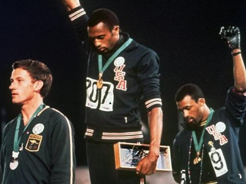 Three athletes on the Olympic podium. Two raise their fists in a Black Power salute.