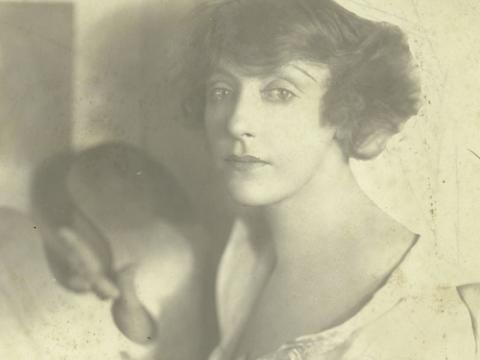 A black and white portrait of Annette Kellerman. She is holding a painting palette with one hand.