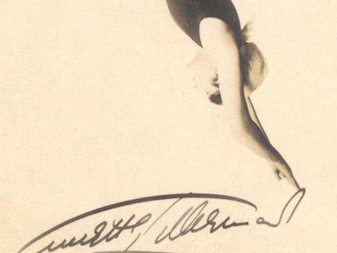 A signed publicity still of Annette Kellerman. She is wearing a figure-hugging swim suit and appears to be diving with her hands pointed downwards. She is on a white background.