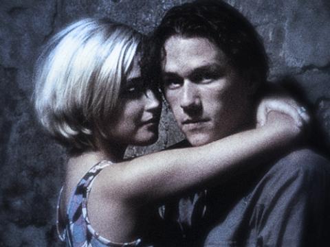Heath Ledger as Jimmy and Rose Byrne as Alex in a still from Two Hands. The shot is grainy and plays with focus. They are in an embrace while they lean on a wall. Ledger looks at the camera.