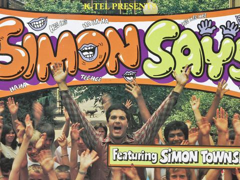 A record sleeve for an album titled Simon Says. On the cover is the title at the top in big flouro-coloured orange and green letters and below that is a picture of Simon Townsend surrounded by kids. Everyone has their hands stretched up in the air.