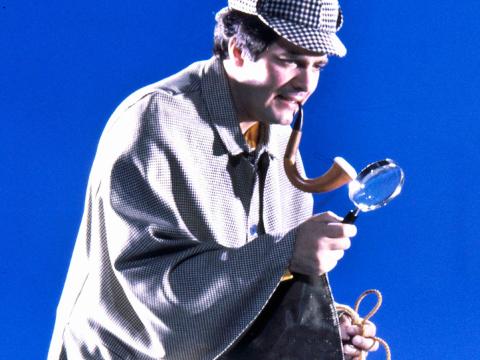 Simon Townsend dressed as Sherlock Holmes looking through a magnifying glass.