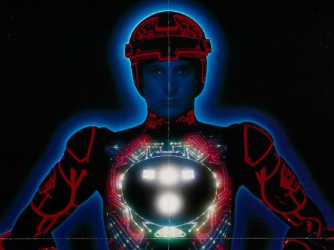 Film poster for the movie Tron showing a man, hands on hips, wearing an illuminated spacesuit and helmet.