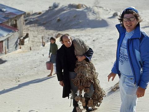 Director Henri Safran standing in the sand dunes with actor Peter Cummins (Hide-Away Tom) above the humpy set from Storm Boy
