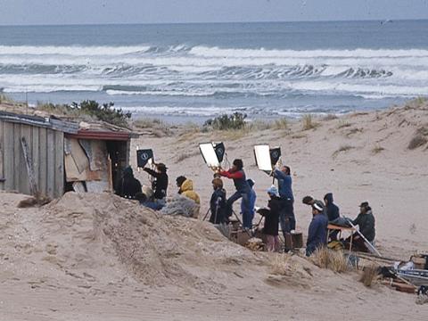 Crew with tall lights film outside the humpy set for the film Storm Boy