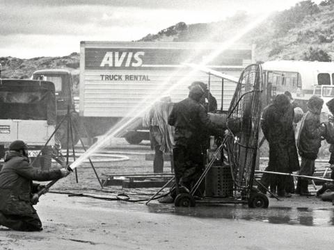 Scene during the shooting of Storm Boy, showing the crew 'making rain' with a hose connected to an off-camera water truck, a wind machine in the centre used to heighten storm effects, an Avis truck in the background which was used to haul heavy duty equip