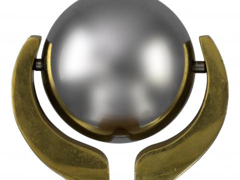 Chrome sphere suspended between two brass arms, mounted on wooden plinth. Gold coloured metal plaques are attached to opposite sides of the plinth.