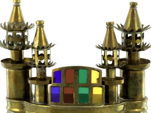 Close up of Brass trophy consisting of four legs, a hollow mid section (with door at rear) and three portals at front, four decorative turrets at top and at centre top, a stained glass feature. 