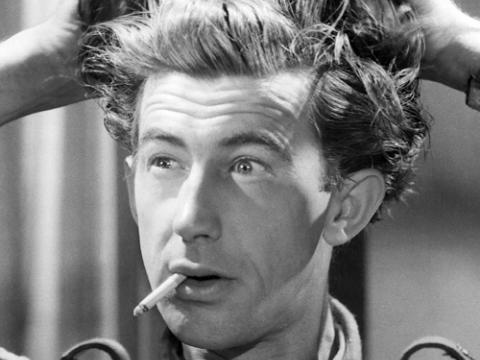 A still of Chips Rafferty holding up his hair with a cigarette hanging out of his mouth.