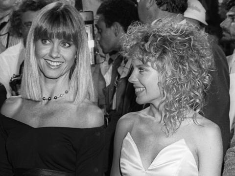 Kylie Minogue stands next to Olivia Newton-John in this black and white photograph.