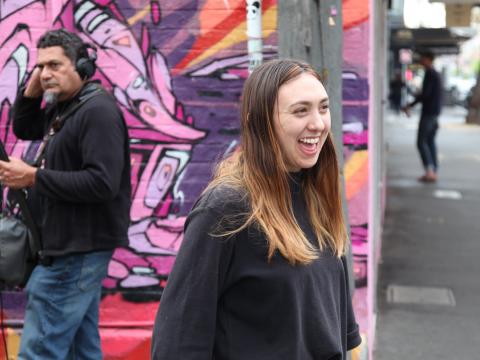 Indigenous performer Alice Skye standing in a Melbourne street with a graffitied wall behind her.