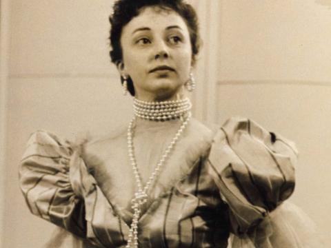 A woman is wearing a costume. She has a pearl necklace and puffy sleeves.