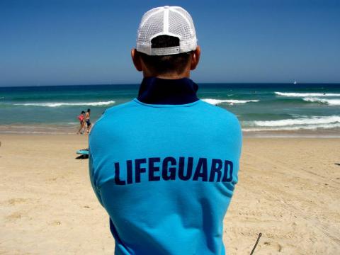 A lifeguard with his back to the camera watches over Bondi Beach