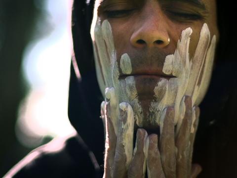 Indigenous man wipes white clay onto his face.