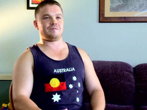 Man wearing a singlet with a print of Indigenous flag inserted where the Union Jack would be on the Australian flag.