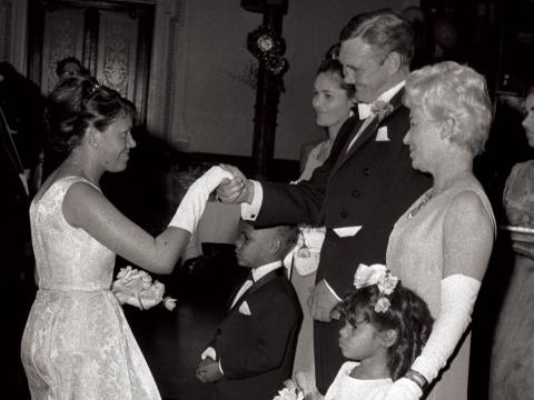 Aboriginal women in a evening gown curtseying to Prime Minister Gorton.