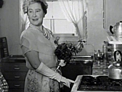 The Queen Mother standing in a kitchen at the stove during a visit to a suburban family home in Villawood in 1958