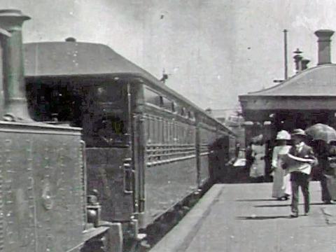 People walking along the platform at Newtown station in Sydney as a train pulls up alongside them in 1899.