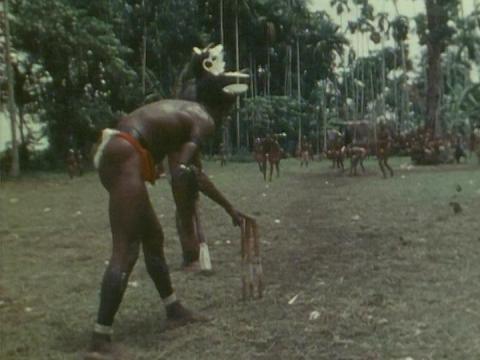 During a Trobriand Island cricket match, the bowler who is wearing traditional dress of war, touches the stumps while he waits for the ball to be returned to him