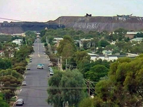 Wide angle shot of a main street in Broken Hill. Houses and trees are seen in the foreground and mines in the background.