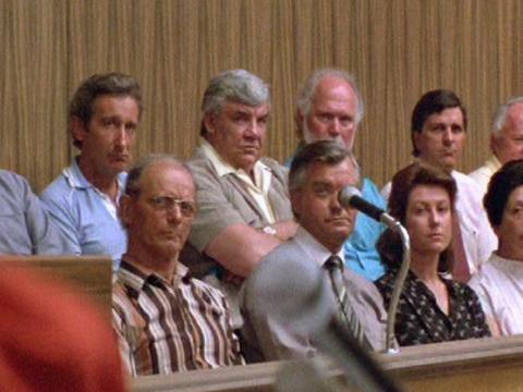 Eleven men and women in the jury box look towards the a judge in the foreground