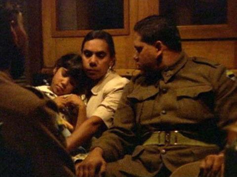 Two men in army greens sitting in a train carriage, one of them next to a woman with her daughter