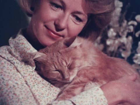 A close up of a woman cuddling a ginger cat.