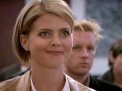 A well-dressed woman at an art auction smiling with other people in the background
