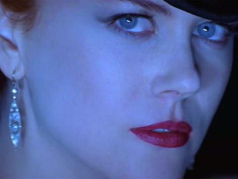 Closeup of Nicole Kidman as Satine looking towards camera in blue-hued lighting wearing diamond earrings and red lipstick