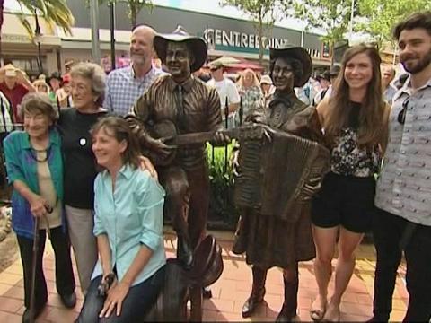 Joy McKean and her family posing for photographs alongside the bronze statue of her and her husband, singer Slim Dusty in Tamworth