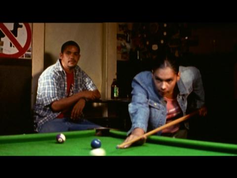 A man and a woman at a pool table, the woman is hitting the cue ball while the man sits in the corner