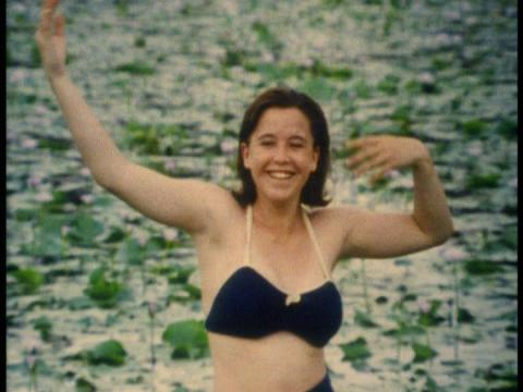 A young girl in swimwear with raised arms in front of the water