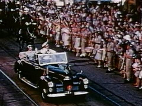 Queen Elizabeth II and Prince Philip in an open car waving at large crowds of people lining the street.