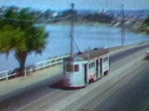 A tram travels along a Brisbane street in the 1960s. The Brisbane River is in the background.