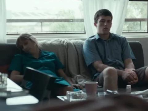 Teenage boy sits watching tv with his mother slumped beside him