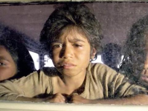 Three Aboriginal girls stare out the back window of a car having just been taken from their mothers