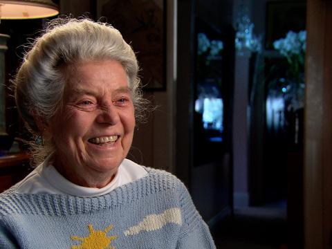 A colour still of Hilarie Lindsay who was a little girl when the Sydney Harbour Bridge opened in 1932. She is smiling as she's recalling the opening of the Harbour Bridge She is wearing a knitted jumper with the Harbour Bridge on it.