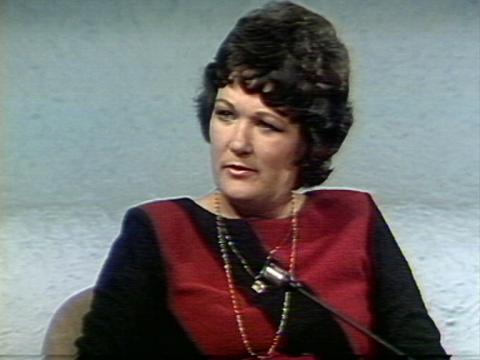 A woman is looking quizically off camera. She is sitting in a studio.
