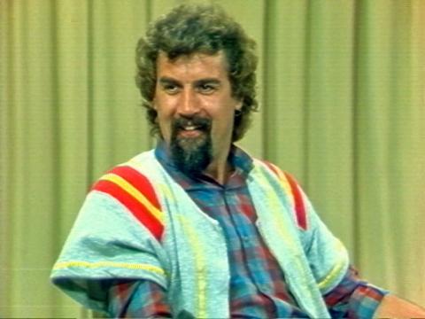 Comedian Billy Connolly is laughing. He is sitting in a studio.
