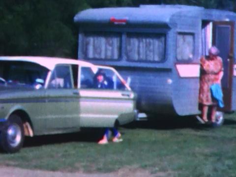 A young girl climbs into the back seat of the family's green Holden while her grandmother exits the door of the caravan.