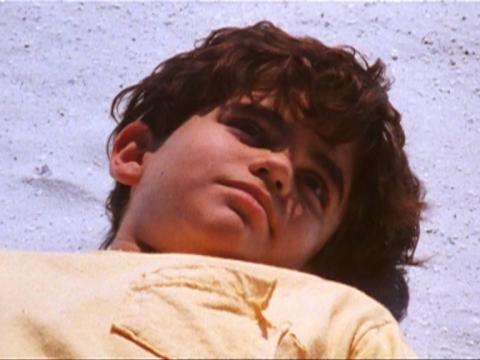 A young boy in a yellow shirt laying unconscious on sand