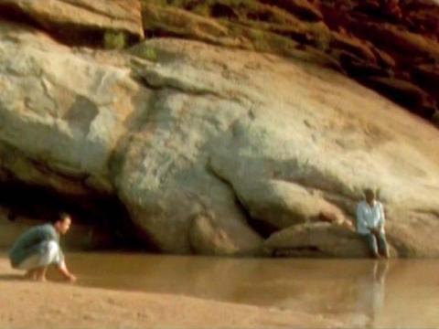 Two people are on either side of a body of water in the desert