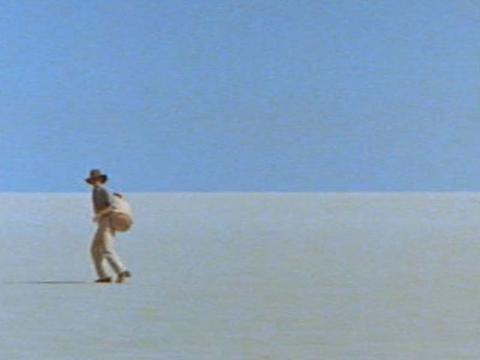 Two men are walking across the desert. We see them from faraway. One lags behind the other.