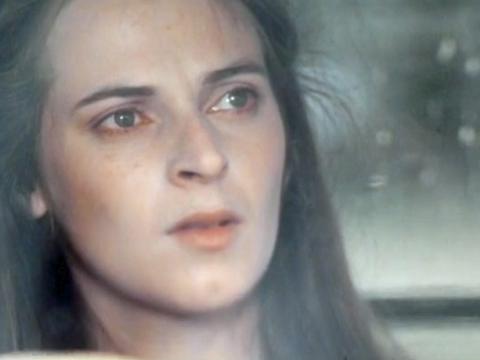 Close up of a woman sitting inside a car with a wet windshield, she's looking into the distance.