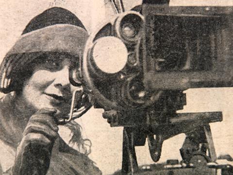 Newspaper image of close up of a woman in 1920s style hat looking into the lens of a movie camera