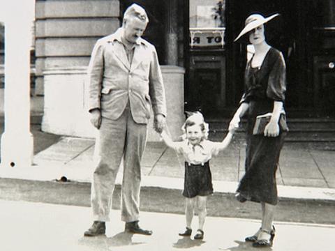 A man and woman from the 1930s holding the hands of a small child who is standing in between them.